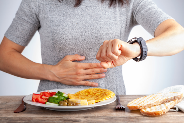 A person checking their watch while holding their stomach, with a plate of food in front, suggesting intermittent fasting.