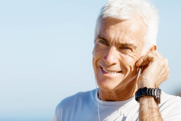 A fit, older, happy man listens to music through earbuds.