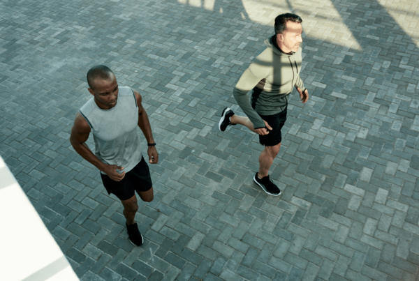 Two middle-aged men jogging along a paved running path in the city.