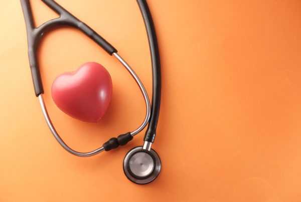 A stethoscope curls on an orange background next to a glossy red heart.