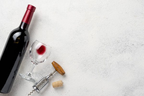 A bottle of wine, a cork screw, and a glass of wine lay on a white marble countertop.