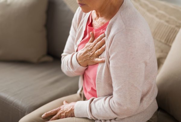 A woman holding her chest during a heartache sits on her couch, wishing she had used Cleerly cardiac imaging.