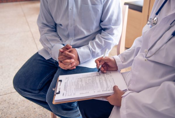 A man sits in his physician’s office while his doctor fills out forms related to his yearly executive physical.
