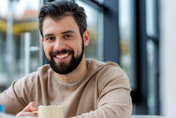 A smiling man with a beard holds a mug of his favorite drink after learning why self care isn’t selfish.