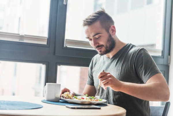 A young man with a beard eats a healthy meal with lots of veggies to give him energy while practicing a fasted lifestyle.