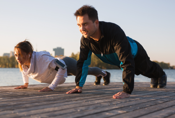 Two people do push-ups together on a wooden dock to get good exercise and grow stronger.