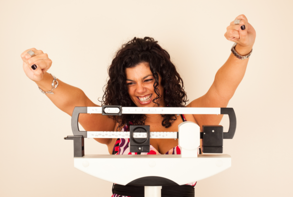 A woman on a weight loss journey is excited while standing on a scale because she reached her target weight.
