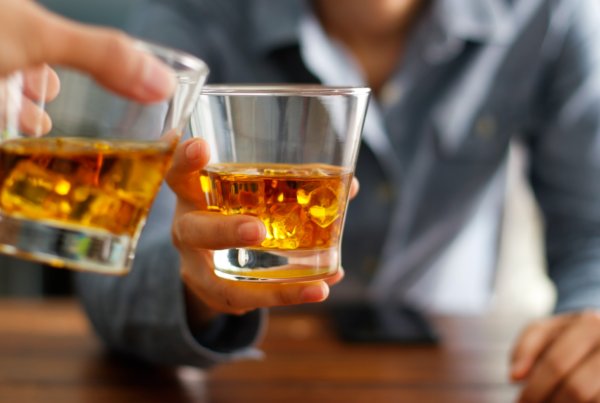 Two people touch their glasses of whiskey together while saying, "Cheers!"