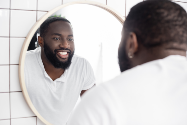 A man smiles at himself in the mirror because he has good self esteem and loves himself.