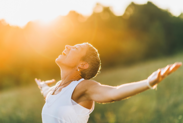 A woman with cropped hair stands smiling with open arms to the sky after learning the connection between spirituality and health.