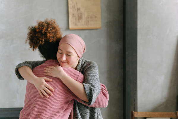 A curly-haired woman hugs her best friend in celebration because she found her breast cancer early enough to treat it.