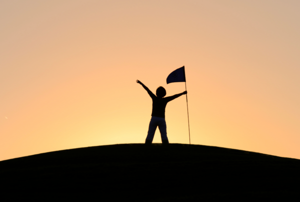 A young person holding a flag stands in celebration in front of the sunset, representing goal setting and discipline.