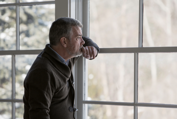 A man leans and stares out of a window, grieving after loss.