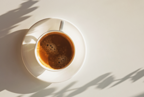 A cup of coffee, as seen from above, rests in a matching saucer on a white table top.