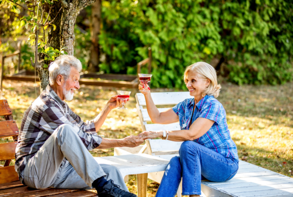 An elderly couple sitting outdoors, toasting with drinks, symbolizing active and joyful retirement living.