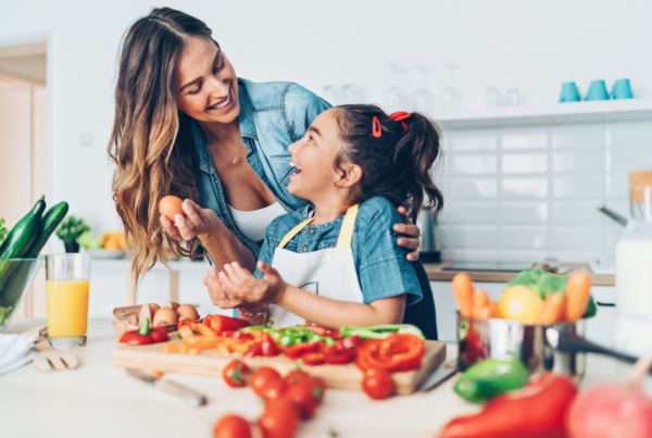 Mother and daughter laughing while preparing healthy ingredients in the kitchen, promoting stress-free parenting.