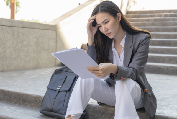 A woman in business attire reads documents with concerned expression while sitting on outdoor steps.