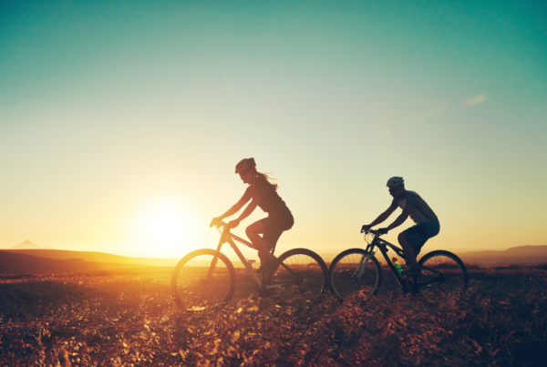 Two cyclists riding mountain bikes on a hilltop trail at sunset.