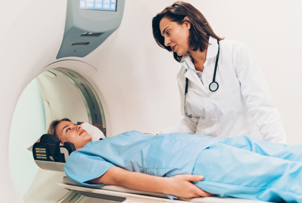 Medical professional in white coat with stethoscope assists patient in hospital gown preparing for MRI examination.