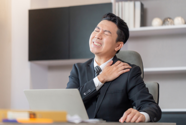 A business professional holding his shoulder, suggesting upper extremity pain or discomfort.