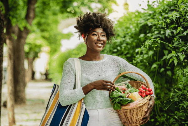 Smiling woman holding basket of fresh vegetables outdoors.