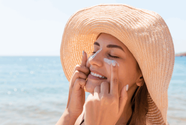 Woman wearing a wide-brimmed straw hat applies white sunscreen to her face.