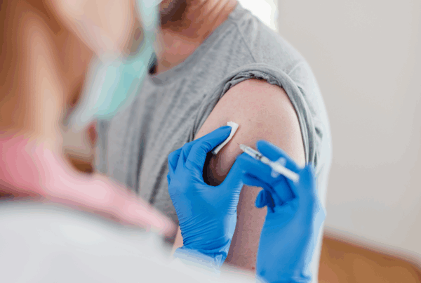 Healthcare professional’s gloved hands administer vaccine injection into patient’s arm.