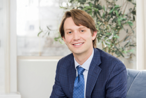 A physician in professional attire sitting in modern, comfortable medical office setting.