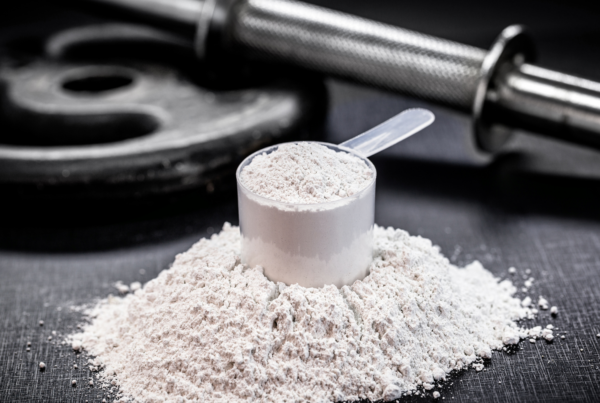 Scoop of creatine monohydrate powder with weight plates and dumbbell in background.