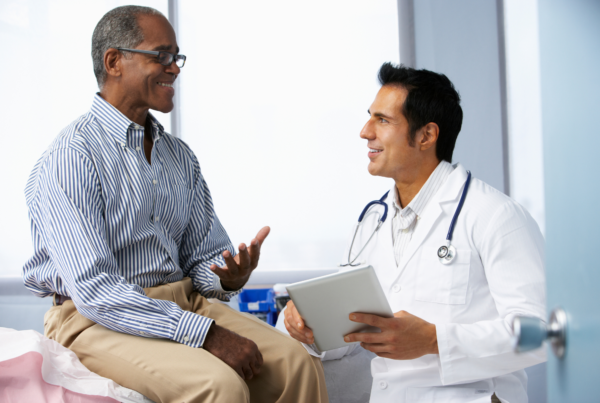Male doctor holding a tablet, discussing an optimal health approach with a middle‑aged male patient.