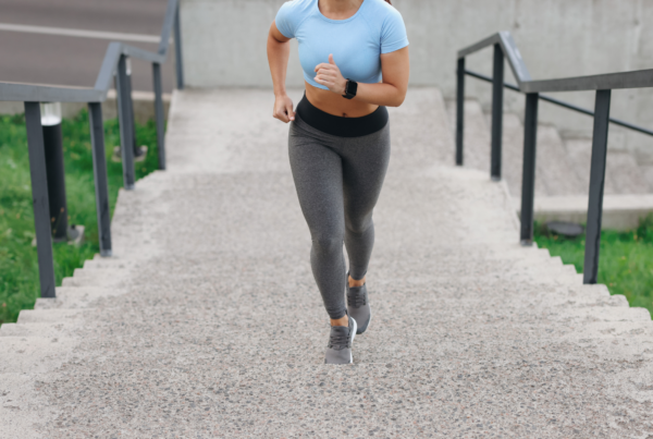 Woman in workout clothes running up outdoor concrete stairs.