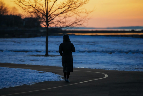 Silhouette of a person walking alone on a path at dusk on snow-covered ground.