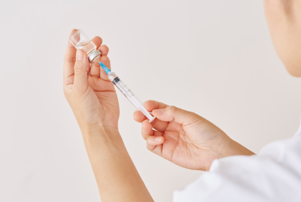 Hands drawing liquid from a small glass vial into a syringe.