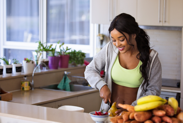 A fit woman in athletic wear prepares fresh fruit and vegetables in a bright kitchen.