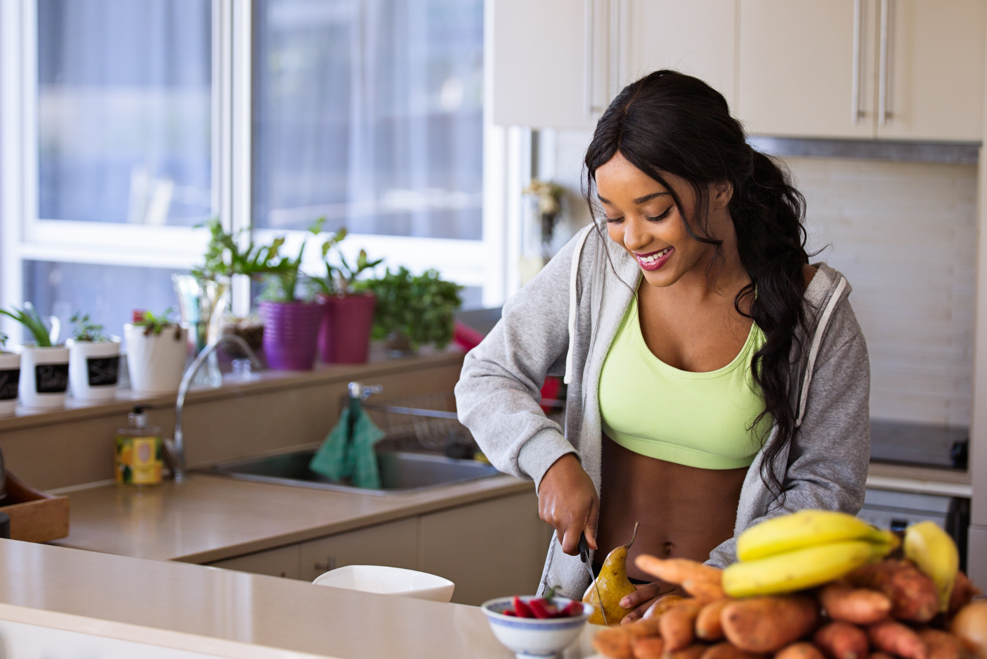 A fit woman in athletic wear prepares fresh fruit and vegetables in a bright kitchen.