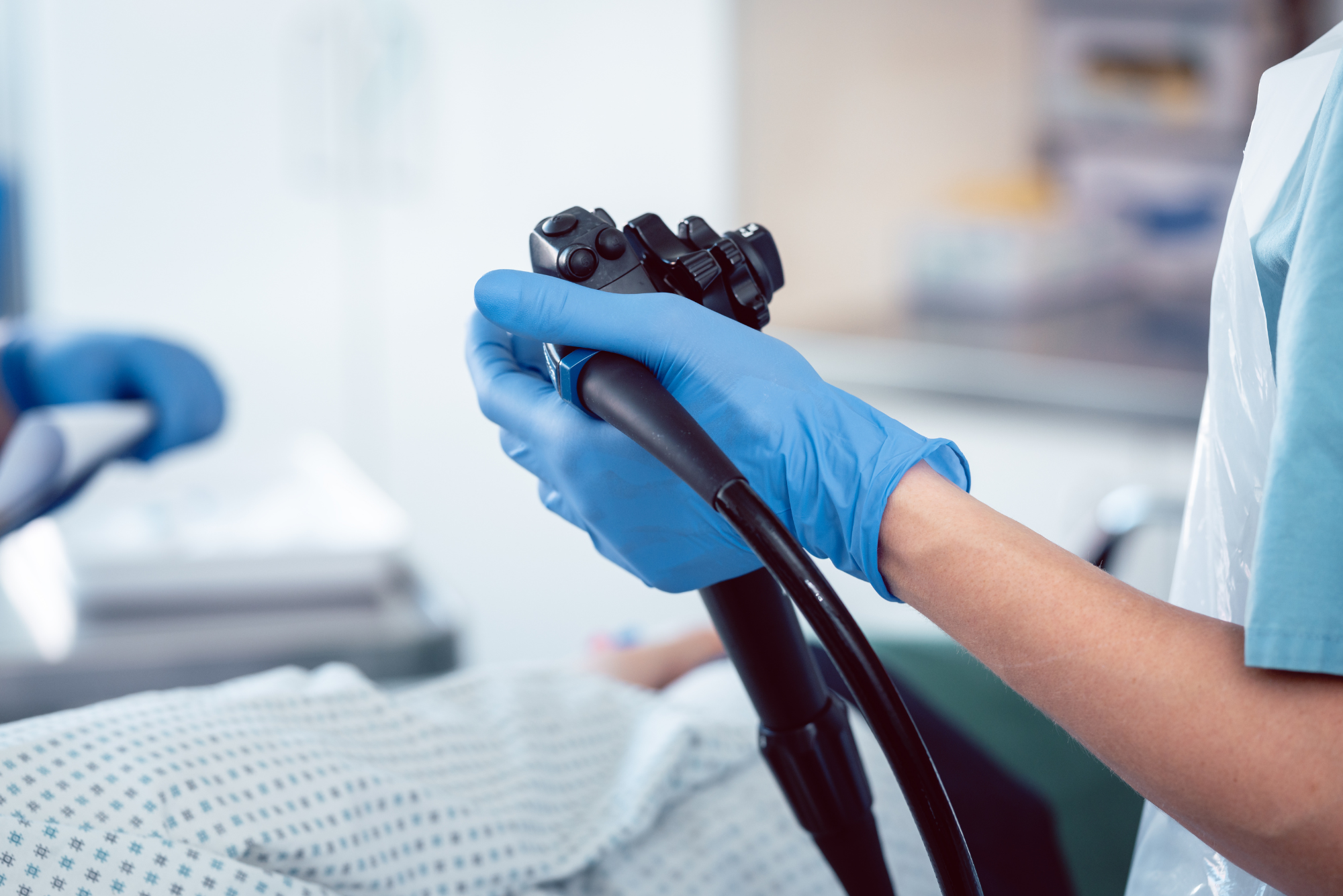 A clinician holds an endoscope before a colonoscopy procedure, with the patient prepped on the exam table.